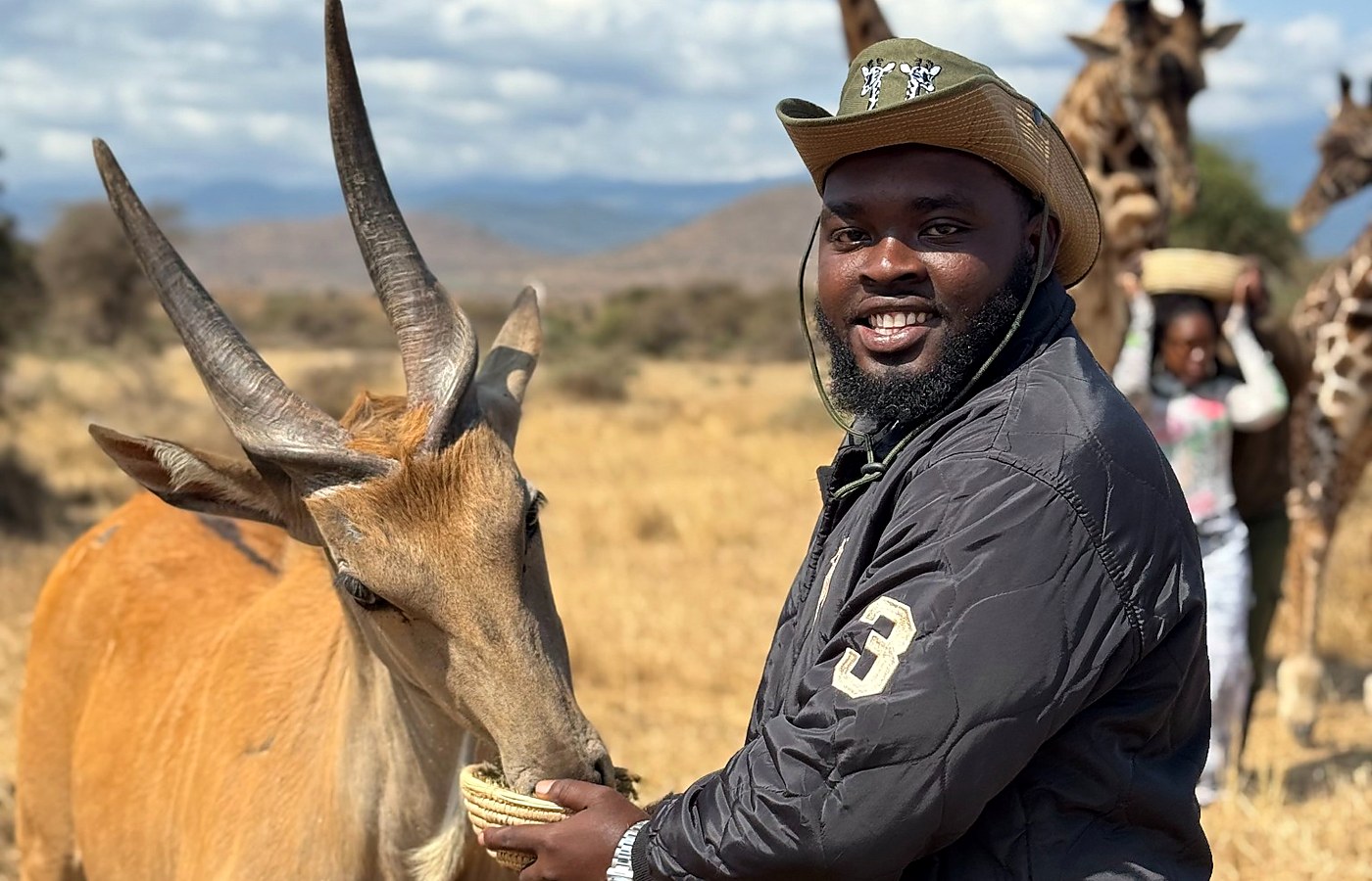 Safari guest feeding an antelope with giraffes in the background